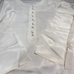 May include: A white long-sleeved shirt with a button-up closure. The shirt is made of a sheer fabric and has a loose fit.