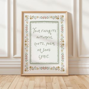 May include: A rectangular framed print featuring the text "YOUR FAVORITE AUTUMNAL QUOTE, POEM, OR SONG LYRIC." The text is centered within a green dotted border, surrounded by a decorative floral pattern in shades of pink, yellow, and green.