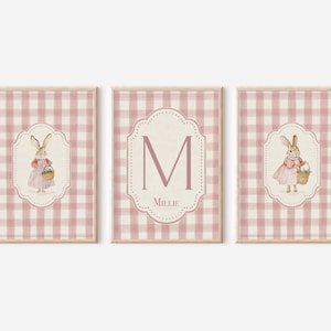 May include: Three framed prints featuring a pink and white gingham pattern. Two prints show a bunny in a dress holding a basket. The center print has the letter "M" and the name "Millie".