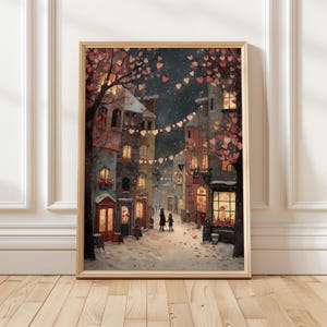 May include: A framed print of a romantic street scene. The artwork depicts a snow-covered street lined with buildings, illuminated by warm light from windows and street lamps. Heart-shaped decorations adorn the trees and overhead strings, creating a cozy, festive atmosphere.