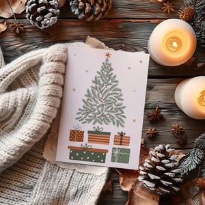 May include: A Christmas card with a green tree and wrapped gifts is displayed on a wooden surface, alongside lit candles, pine cones, and a cozy cream-colored sweater. Festive holiday decor.