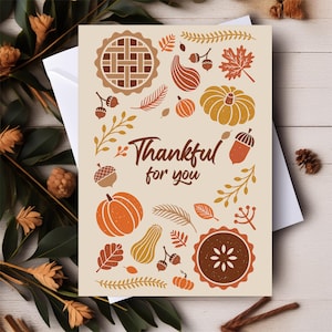 May include: Thanksgiving greeting card with a cream background and fall-themed illustrations. The card features pumpkins, leaves, acorns, and pie, with the text "Thankful for you" in brown script. The card is inside a white envelope.