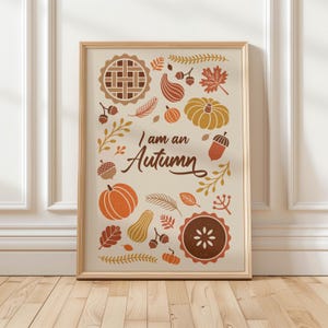 Puede incluir: Una lámina decorativa enmarcada con fondo crema y el texto "I am an Autumn" en letra cursiva marrón. El diseño incluye ilustraciones de calabazas, tartas, bellotas, hojas y ramas en tonos naranja, amarillo y marrón.