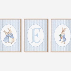 Puede incluir: Tres impresiones enmarcadas a rayas azules y blancas con ilustraciones de Peter Rabbit. La primera impresión muestra dos Peter Rabbits abrazándose. La segunda impresión tiene la letra E en un círculo azul. La tercera impresión muestra a Peter Rabbit sosteniendo una zanahoria.