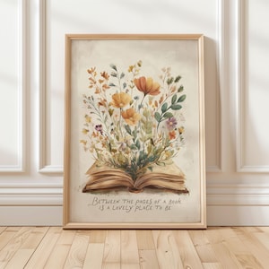 Peut inclure: Une impression encadrée à l'aquarelle représentant un livre ouvert avec des fleurs et du feuillage colorés jaillissant de ses pages. L'œuvre d'art a une esthétique vintage, avec le texte "Between the pages of a book is a lovely place to be."