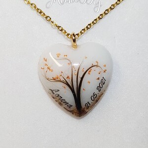 May include: A heart-shaped pendant necklace with a gold chain. The pendant is white with a tree design and gold accents. The name "Lorena" and the date "21.05.2021" are inscribed on the pendant.