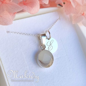 May include: A silver necklace with two pendants. One pendant is a small, round, clear stone with hair inside. The other pendant is a small, round silver disc with the letter "E" engraved on it. The necklace is displayed in a white box.