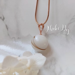 May include: A white and gold pendant necklace with a round, white orb pendant with gold swirls. The necklace is on a rose gold chain.