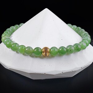 May include: A green jade stone bracelet with a gold bead accent. The bracelet is made of round beads and is displayed on a white surface.