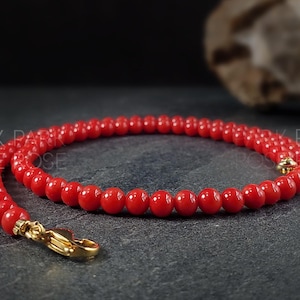 Könnte beinhalten: Eine rote Korallenkette mit einem goldenen Verschluss. Die Kette besteht aus kleinen, runden Perlen.