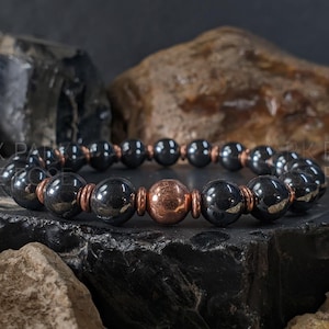 May include: A beaded bracelet featuring polished dark grey spherical beads alternating with smaller copper-toned spacers and a single larger central copper-toned bead. The text PARK ROSE is visible on the left and right sides of the image.