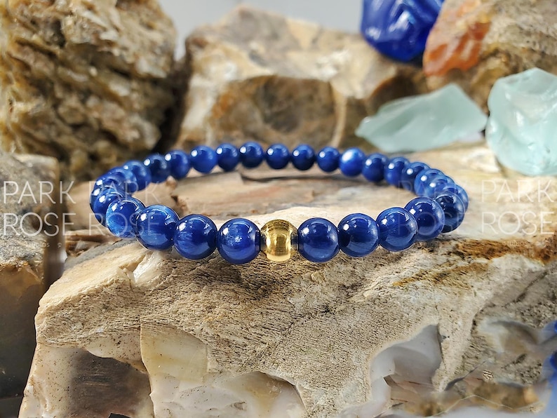 May include: A blue gemstone bracelet with a gold bead accent. The bracelet is made of round beads and is strung on a stretchy cord.