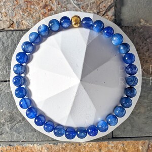 May include: A blue gemstone bracelet with gold accents. The bracelet is made of round beads and is strung on a stretchy cord.