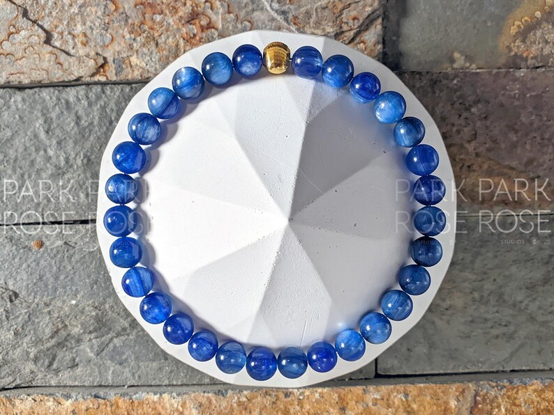 May include: A blue gemstone bracelet with gold accents. The bracelet is made of round beads and is strung on a stretchy cord.