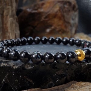 May include: Black beaded bracelet with a gold bead accent. The bracelet is made of black gemstone beads and a single gold bead.