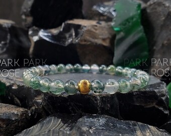 May include: A green moss agate bracelet with a gold bead accent. The bracelet is made of natural stones and is a beautiful and unique piece of jewelry.