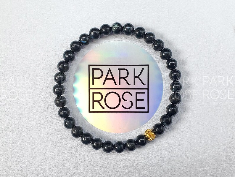 May include: A black beaded bracelet with a gold accent. The bracelet is on a white background with a holographic sticker that says "PARK ROSE".