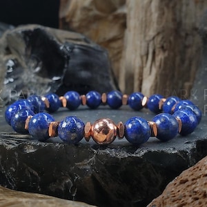 Puede incluir: Un brazalete de cuentas azules y cobre con una cuenta de acento de cobre. El brazalete está hecho con cuentas de lapislázuli y cobre.