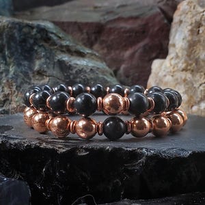 May include: Two bracelets made of black and copper beads. The bracelets are stacked on top of each other.