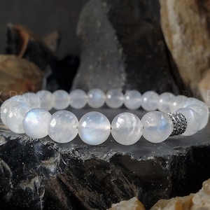 Op de afbeelding: Een witte maanstenen armband met een zilveren sluiting. De armband is gemaakt van ronde kralen en ligt op een donkere achtergrond.