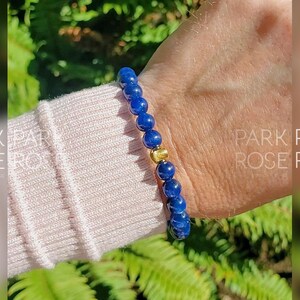 May include: A blue gemstone bracelet with a gold bead accent. The bracelet is on a person's wrist.