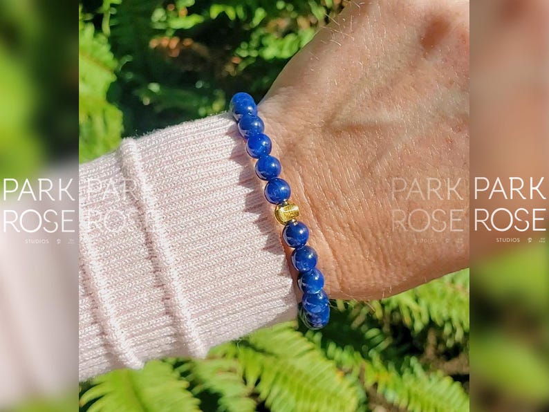 May include: A blue gemstone bracelet with a gold bead accent. The bracelet is on a person's wrist.