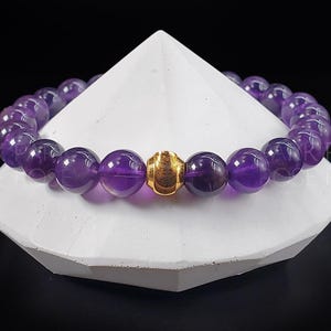 May include: A purple amethyst gemstone bracelet with a gold bead accent.