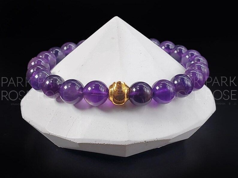 May include: A purple amethyst gemstone bracelet with a gold bead accent.