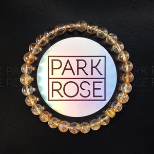 May include: A gold gemstone bracelet with a Park Rose logo tag. The bracelet is made of round beads and is a light gold color.