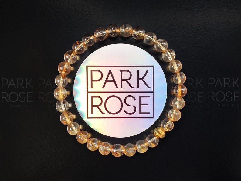 May include: A gold gemstone bracelet with a Park Rose logo tag. The bracelet is made of round beads and is a light gold color.