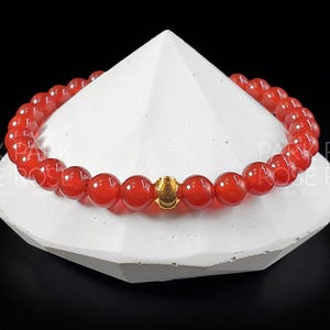 May include: A red carnelian gemstone bracelet with a gold accent bead.