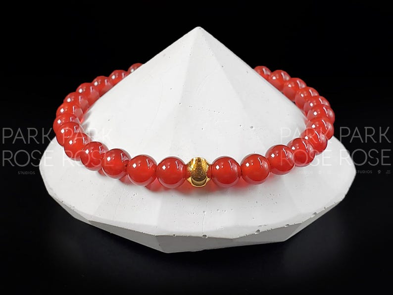 May include: A red carnelian gemstone bracelet with a gold accent bead.