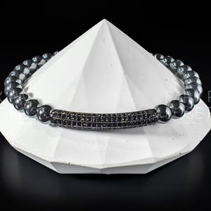 May include: A black beaded bracelet with a silver bar set with black stones.