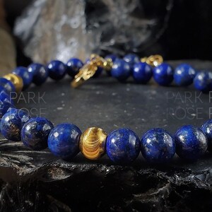 May include: A blue lapis lazuli beaded bracelet with gold accents. The bracelet has a clasp and a decorative gold bead.