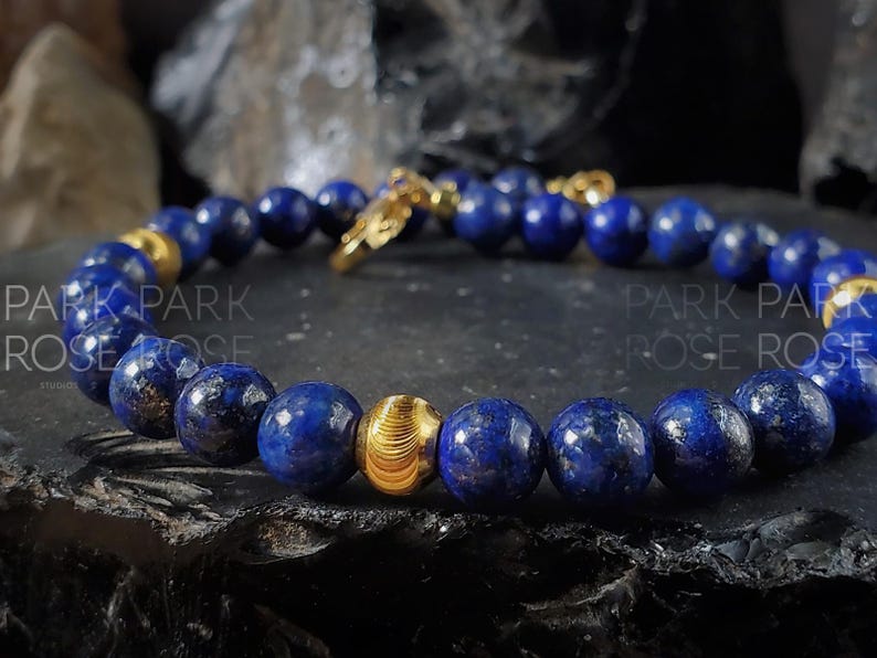 May include: A blue lapis lazuli beaded bracelet with gold accents. The bracelet has a clasp and a decorative gold bead.
