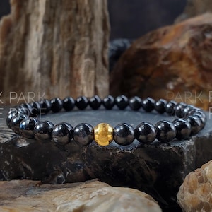 May include: A black onyx beaded bracelet with a single gold bead accent. The bracelet is on a dark background.