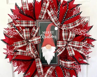 Puede incluir: Una corona navideña festiva con un diseño de gnomo. La corona presenta malla roja, cintas a cuadros y detalles en negro. Un letrero central muestra una ilustración de gnomo y las palabras "Merry Christmas".