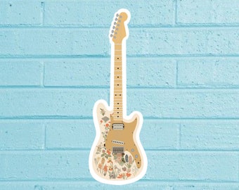 Op de afbeelding: Een vintage-stijl elektrische gitaar met een bloemenpatroon. De gitaar is crèmekleurig met een bruine houten hals en een bloemenpatroon op de body. De gitaar heeft een enkele pickup en een tremolobar.