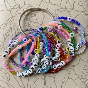 May include: A collection of colorful beaded bracelets with letter beads spelling out words like "FEARLESS", "LOVE", "NOW", and "BRIGHT".