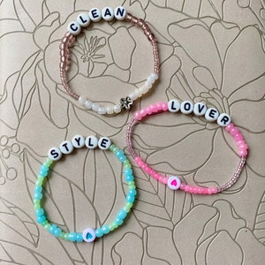 May include: Three beaded bracelets with white letter beads spelling out "CLEAN", "LOVER", and "STYLE". Each bracelet has a small white heart charm.