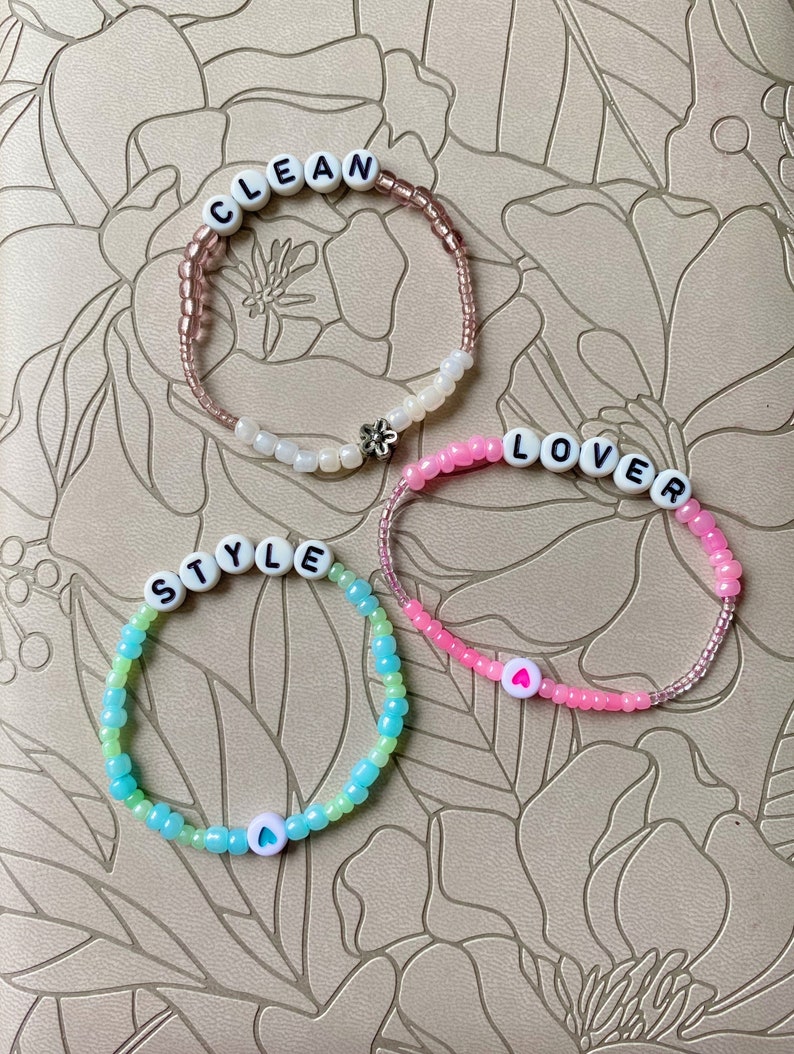 May include: Three beaded bracelets with white letter beads spelling out "CLEAN", "LOVER", and "STYLE". Each bracelet has a small white heart charm.