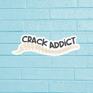 May include: A sticker with a white spine and the text "CRACK ADDICT" in black letters.