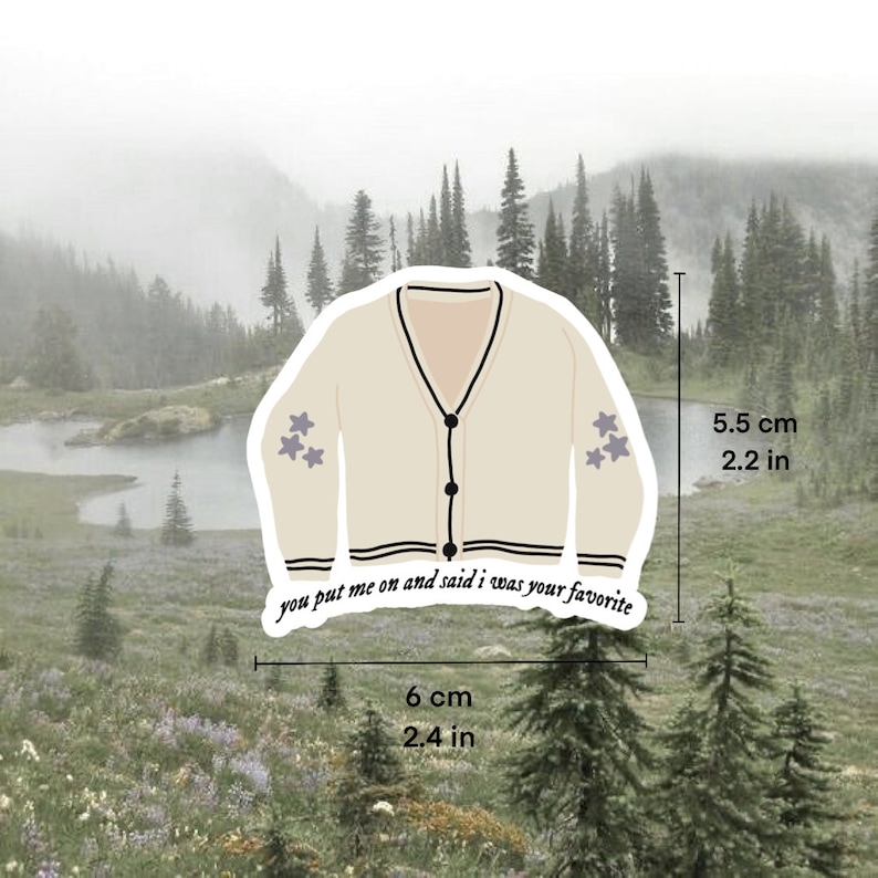 May include: A beige cardigan with black trim and three purple stars on each sleeve. The cardigan has a button closure and the text "you put me on and said i was your favourite" is printed on the bottom. The cardigan is 6 cm wide and 5.5 cm tall.