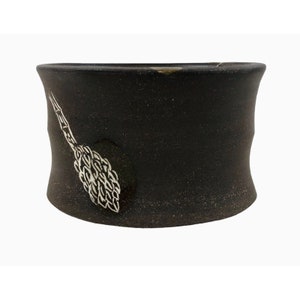 May include: A black ceramic planter with a white design of a stylized pine cone.