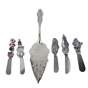 Può includere: Una collezione di utensili da portata natalizi argentati. Include un server per torte con testo "Let it Snow", uno spalmatore a pupazzo di neve e spalmatori con disegni di Babbo Natale e foglie. Arredamento festivo natalizio.