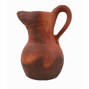 May include: A small, brown clay pitcher with a rounded body and a handle. The pitcher has a rustic, handmade look.