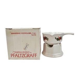 May include: A white ceramic simmering potpourri set with a handle, decorated with red and green floral accents. The set includes a stand and a box with the text "Christmas Heritage by Pfaltzgraff".