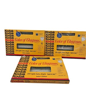 Puede incluir: Tres cajas de luces de Navidad Kodak Color of Christmas 100 luces extra brillantes para añadir en interiores y exteriores. Las cajas son amarillas con texto negro y una imagen verde y blanca de las luces.
