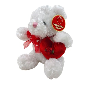 May include: White plush teddy bear holding a red heart with a rose on it. The bear has a pink nose and a red ribbon around its neck. The tag on the bear says "Valentine Bear".