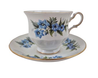 May include: A white teacup and saucer set with a blue floral pattern. The cup and saucer have a gold trim.